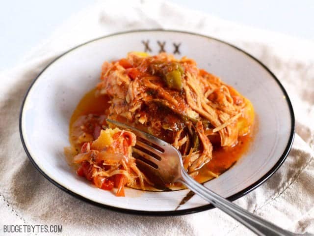 Slow Cooker Italian Chicken and Peppers is an easy dish that can be used multiple ways. Cook up a batch and use it throughout the week! Budetbytes.com Slow Cooker Italian Chicken and Peppers on polenta with a fork taking a bite