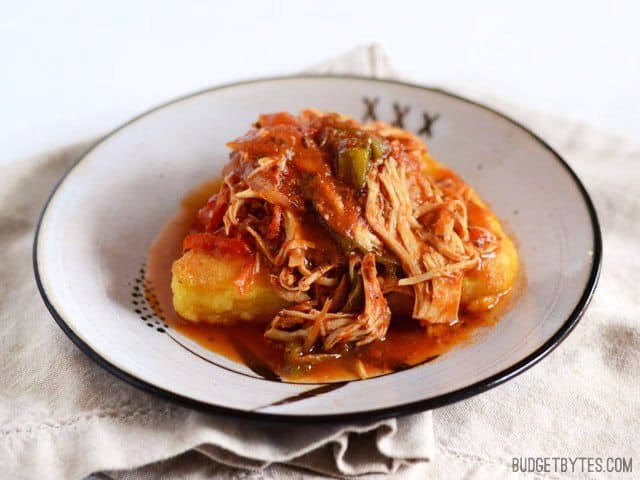 Slow Cooker Italian Chicken and Peppers is an easy dish that can be used multiple ways. Cook up a batch and use it throughout the week! Budetbytes.com Slow Cooker Italian Chicken and Peppers spooned over a slice of polenta on a plate
