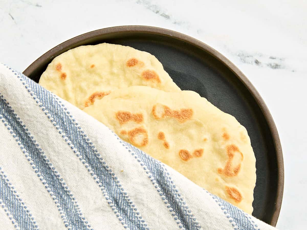 Soft, pillowy, homemade naan bread is easier to make than you think and it's great for sandwiches, pizza, dipping into soups and sauces, and more. Budgetbytes.com Two freshly cooked naan on a plate being covered with a kitchen towel.