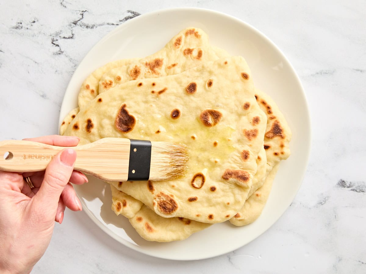 Soft, pillowy, homemade naan bread is easier to make than you think and it's great for sandwiches, pizza, dipping into soups and sauces, and more. Budgetbytes.com Homemade naan being brushed with melted butter.