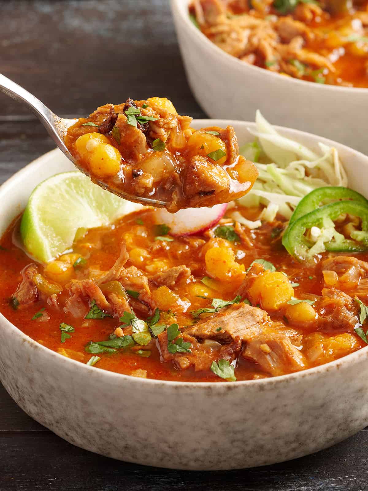 Side view of a bowl of 30 minute posole with a spoon taking some from the bowl.