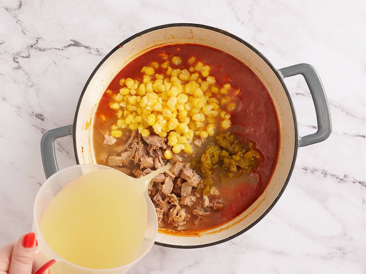 Shredded pork, green chili, hominy, and broth added to a pot to make posole.