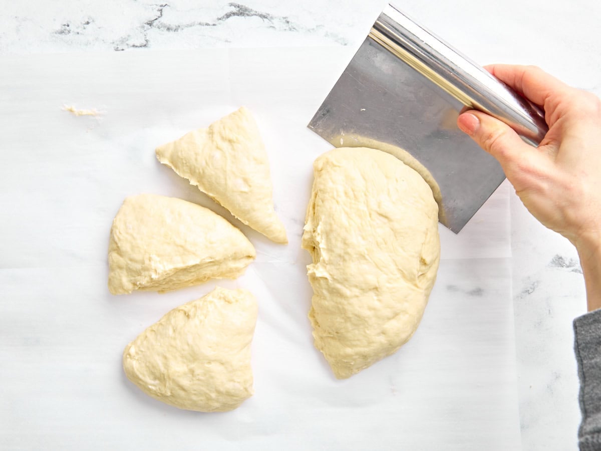 A hand separating naan bread dough into 8 pieces.