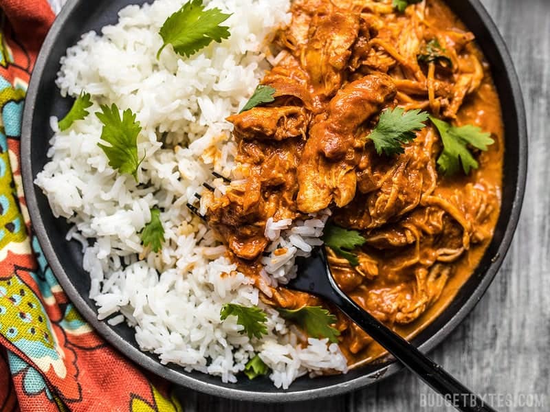 This Slow Cooker Chicken Tikka Masala boasts a rich and aromatic sauce, and tender juicy chicken. Make four servings for the price of one take out! Budgetbytes.com Close up view of Slow Cooker Chicken Tikka Masala on a plate with rice.