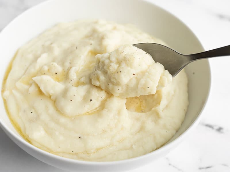 Slow cooker mashed potatoes are the perfect hands-off method for making rich and creamy mashed potatoes for the Holidays! Budgetbytes.com Slow cooker mashed potatoes in a bowl with a spoon lifting a bite