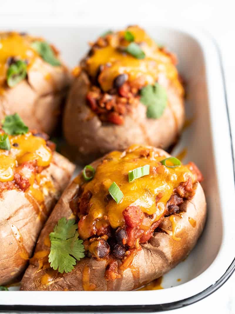 Tender baked sweet potatoes smothered with turkey and bean chili, then topped with melty cheddar. Turkey Chili Smothered Sweet Potatoes are an easy dinner! BudgetBytes.com Front view of four turkey chili stuffed sweet potatoes in a small white baking dish
