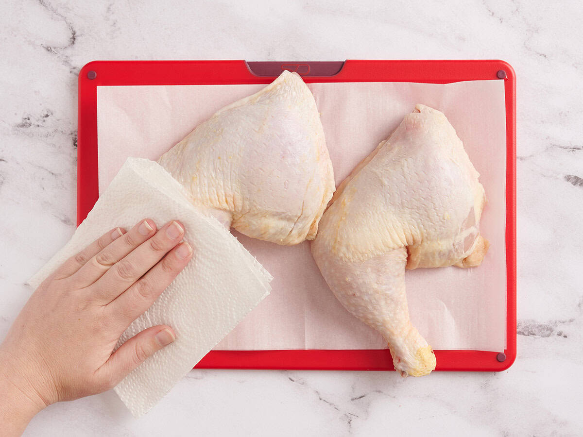 A hand patting a chicken leg dry with a paper towel.