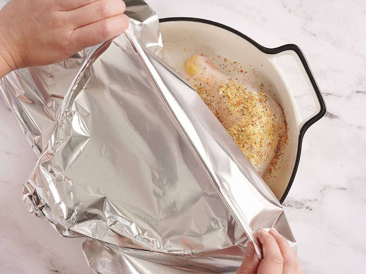 Hands covering a dish of two chicken legs with foil.