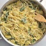 Parmesan cheese being added to a dish of spinach artichoke pasta.