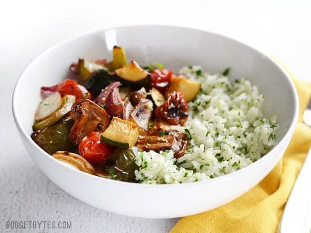 Broiled balsamic vegetables top a vibrant and fresh lemon parsley rice to make this light and healthy dish. Works great as a side or a light meal. Budetbytes.com Broiled Balsamic Vegetables served over lemon parsley rice, in a bowl, sitting on a yellow napkin. Side view.