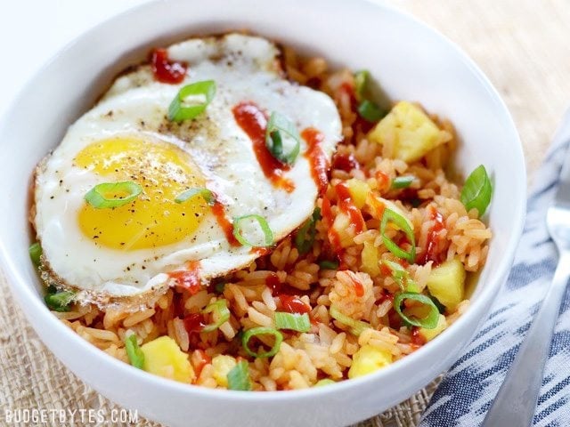Use up the leftovers in your fridge with these fast and tasty Pineapple Sriracha Breakfast Bowls. Easy and customizable to fit what you have on hand. Budetbytes.com Side view of a Pineapple Sriracha Breakfast Bowls garnished with sriracha and green onion, a fork on the side