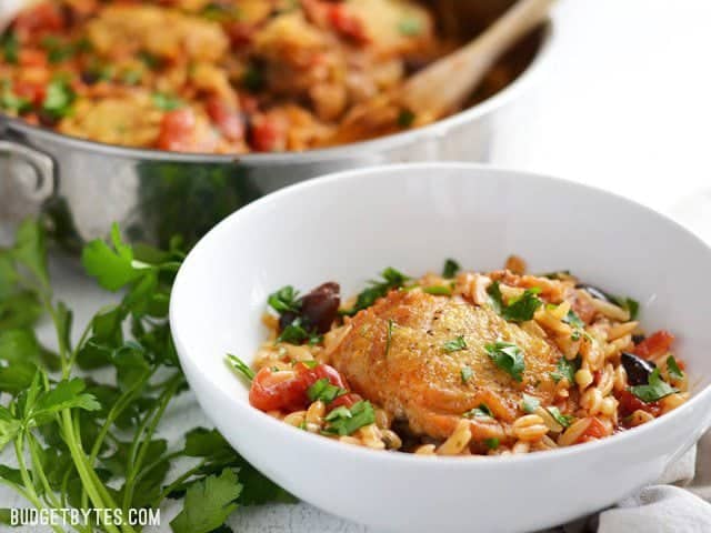This Chicken with Orzo and Olives simmers together in one skillet for maximum flavor and minimum cleanup. A one-pot easy weeknight dinner! Budetbytes.com A bowl of chicken with orzo and olives, the skillet in the background