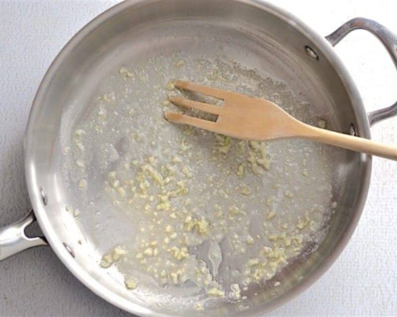 Sauteeing garlic in a skillet with a wooden spoon.