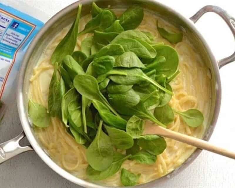 Adding spinach to the pot of pasta and sauce.