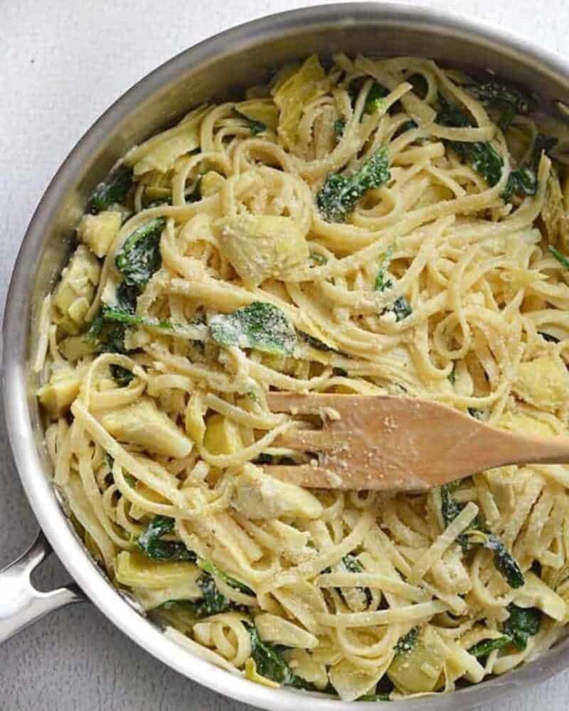 Creamy Spinach Artichoke Pasta in a pot with a wooden spoon.