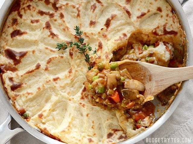 A colorful medley of vegetables, protein filled lentils, and a rich brown gravy make this Vegetarian Shepherd's Pie filling and flavorful without meat. Budetbytes.com Close up of Vegetarian Shepherd's Pie in the skillet, a wooden spoon scooping out a serving