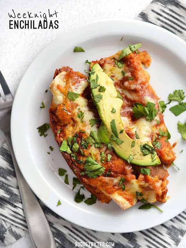 These easy Bean and Cheese Enchiladas are anything but boring. A few extra details take them from a simple to spectacular weeknight dinner. BudgetBytes.com Two Weeknight Bean and Cheese Enchiladas on a plate, garnished with avocado and cilantro.