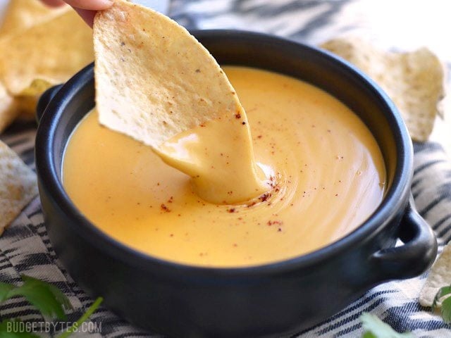 This rich and tangy nacho cheese sauce only takes about 5 minutes to make and uses only real, simple ingredients. Chip dipping into a bowl of rich and creamy 5 Minute Nacho Cheese Sauce