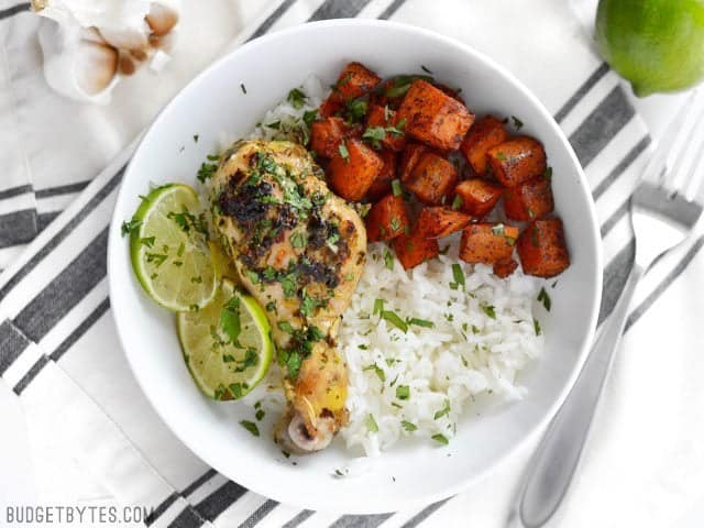 These garlicky Cilantro Lime Chicken Drumsticks are like a blast of summer to get you through those winter blues. Also great for the grill! Cilantro Lime Chicken Drumstick meal in a bowl with rice and sweet potatoes