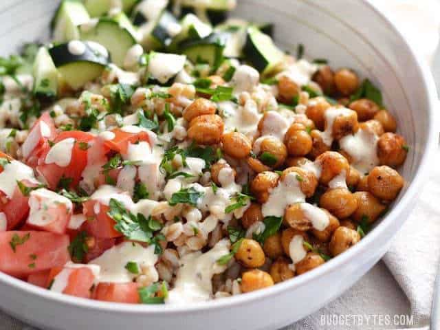 This Mediterranean Farro Salad with Spiced Chickpeas is a flavorful and filling vegan meal packed with tons of fiber and nutrients. Perfect for meal prep! Budetbytes.com Close up side view of a bowl full of Mediterranean Farro Salad