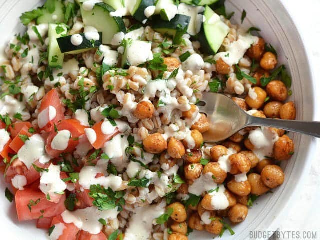 This Mediterranean Farro Salad with Spiced Chickpeas is a flavorful and filling vegan meal packed with tons of fiber and nutrients. Perfect for meal prep! Budetbytes.com Close up overhead view of Mediterranean Farro Salad with Spiced Chickpeas in a bowl, a fork in the center