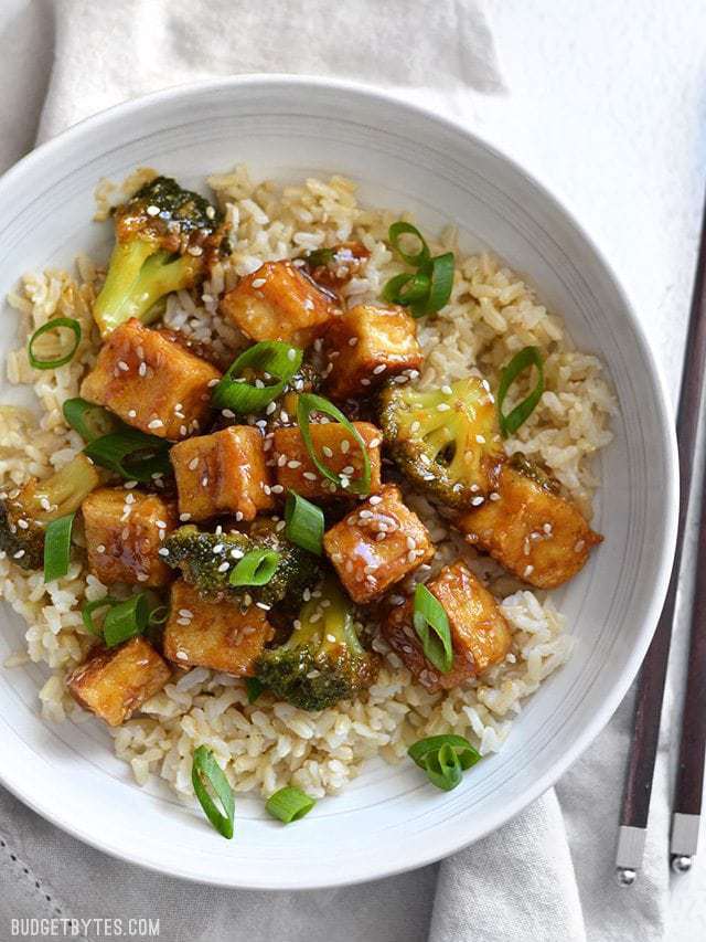This Pan Fried Sesame Tofu is seriously crispy and drenched in a tangy sesame sauce. Broccoli florets and cooked rice make it a meal. Step by step photos. Budgetbytes.com Overhead view of Pan Fried Sesame Tofu with Broccoli in a white bowl.