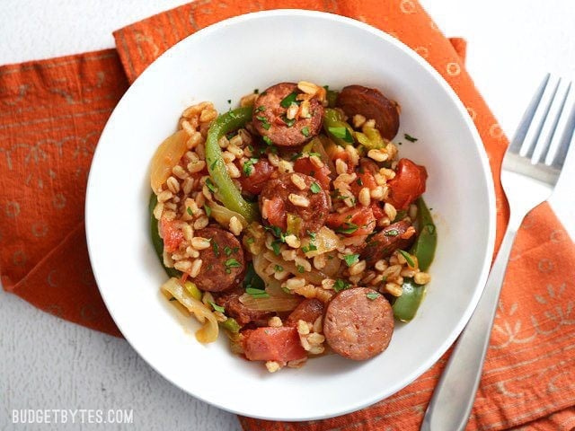 Use farro or any cooked grain in this simple and satisfying weeknight meal. Smoked Sausage with Peppers is a classic flavor combination that always wins! Budetbytes.com Smoked sausage and peppers with farro served in a bowl, on an orange napkin, fork on the side
