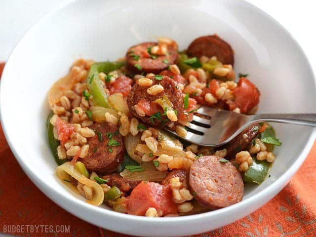 Use farro or any cooked grain in this simple and satisfying weeknight meal. Smoked Sausage with Peppers is a classic flavor combination that always wins! Budetbytes.com Side view of a bowl full of smokes sausage with peppers, onions, and farro. A fork in the middle