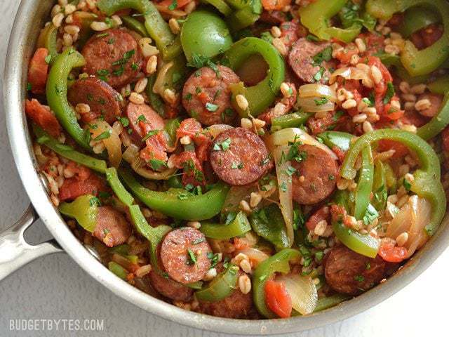 Use farro or any cooked grain in this simple and satisfying weeknight meal. Smoked Sausage with Peppers is a classic flavor combination that always wins! Budetbytes.com Close up overhead view of a skillet full of smoked sausage with peppers, onions, and farro.