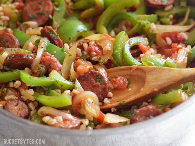 Use farro or any cooked grain in this simple and satisfying weeknight meal. Smoked Sausage with Peppers is a classic flavor combination that always wins! Budetbytes.com Close up of smoked sausage with peppers and farro in the skillet with a wooden spoon