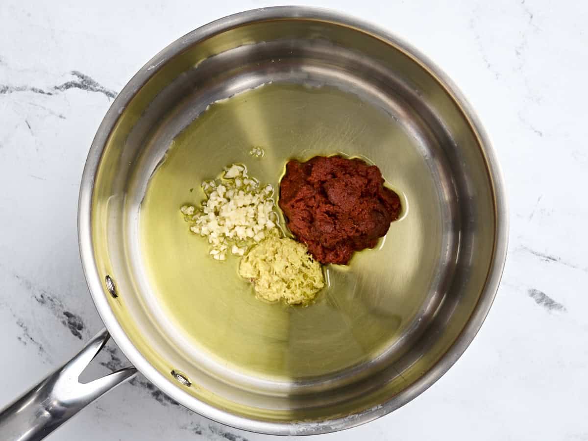 Thai red curry paste, garlic, and ginger in a pan with cooking oil.