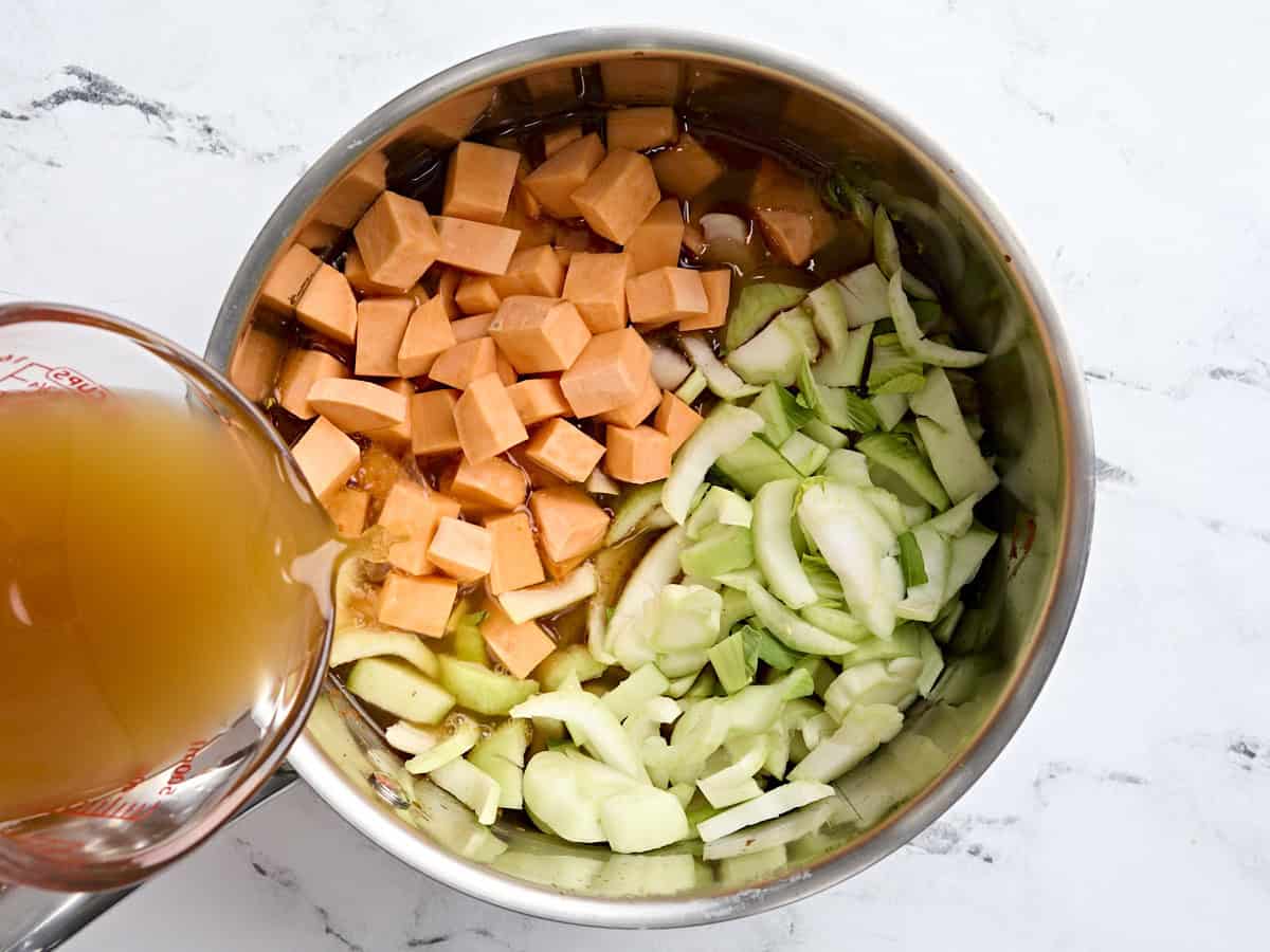Diced sweet potato, bok choy in a pan, with broth being poured on top.