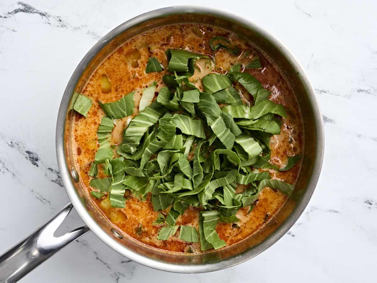 Bok choy leaves added to a pot of red curry vegetable soup.