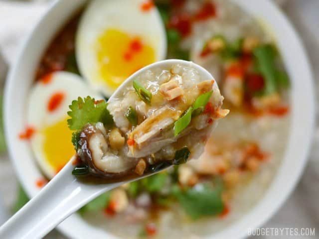 Instant Pot Congee is a warm and comforting rice porridge with endless possibilities for fun toppings. This classic dish is made easy with modern equipment. BudgetBytes.com Close up of a spoonful of congee with toppings, the bowl in the background