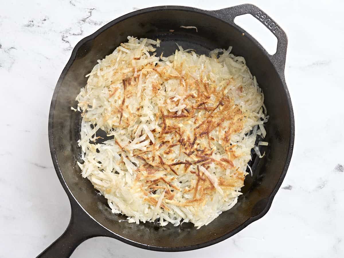 Hashbrowns cooking in a cast iron skillet.