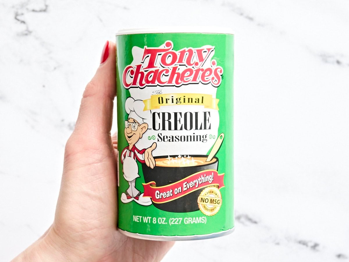 A hand holding a pot of tony chachere creole seasoning.