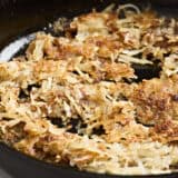 Side view close up of crispy hashbrowns cooking in a skillet.