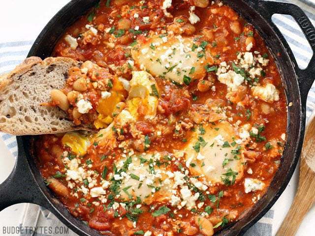 Eggs poached in a rich and smoky tomato sauce speckled with white beans, this Smoky White Bean Shakshuka is a filling and inexpensive breakfast or dinner! BudgetBytes.com A piece of bread dipping into a runny yolk in a skillet full of Smoky White Bean Shakshuka