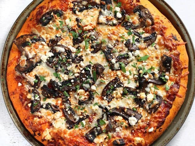 Make this gourmet homemade Portobello Mushroom Pizza for a fraction of the price of take out! Use homemade dough for the best value, or store bought for convenience. BudgetBytes.com Baked Ultimate Portobello Mushroom Pizza not yet sliced, garnished with parsley