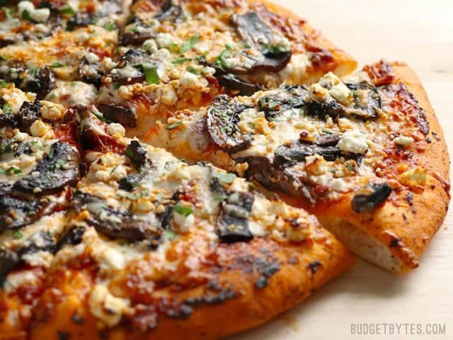 Make this gourmet homemade Portobello Mushroom Pizza for a fraction of the price of take out! Use homemade dough for the best value, or store bought for convenience. BudgetBytes.com Side view of an Ultimate Portobello Mushroom Pizza with one slice pulled slightly out from the rest