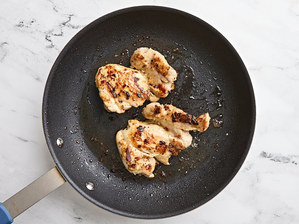 Chicken thighs cooking in a skillet.