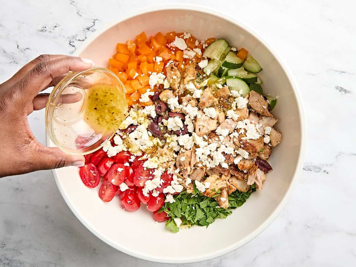Feta cheese added to the ingredients for Greek chicken salad, with the remaining lemon marinade being poured on top.