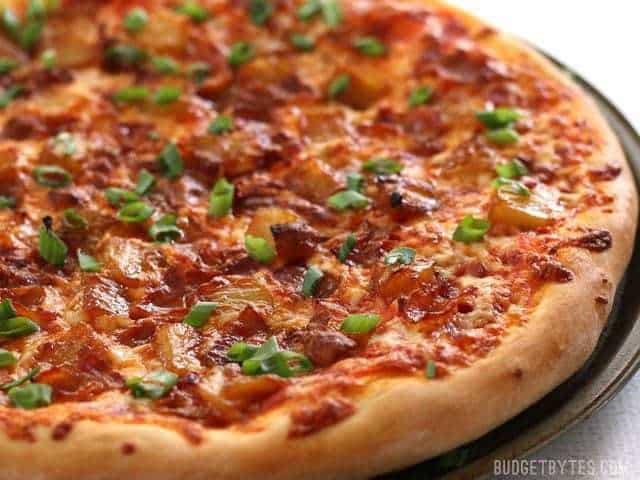 Bacon and Caramelized Pineapple Pizza is the best pizza topping combination for those who love sweet and salty flavors together in one bite! BudgetBytes.com Side view of the baked bacon pizza topped with green onions and pineapple