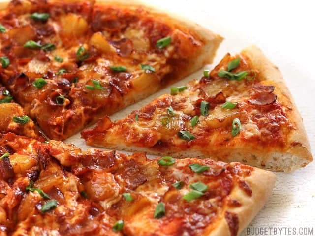 Bacon and Caramelized Pineapple Pizza is the best pizza topping combination for those who love sweet and salty flavors together in one bite! BudgetBytes.com Side view of Bacon Pizza with caramelized pineapple and green onion, one slice pulled out