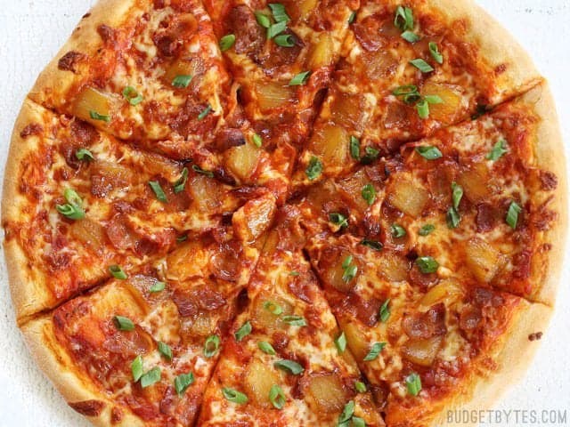 Bacon and Caramelized Pineapple Pizza is the best pizza topping combination for those who love sweet and salty flavors together in one bite! BudgetBytes.com Overhead view of the sliced Bacon Pizza with Caramelized Pineapple and green onion