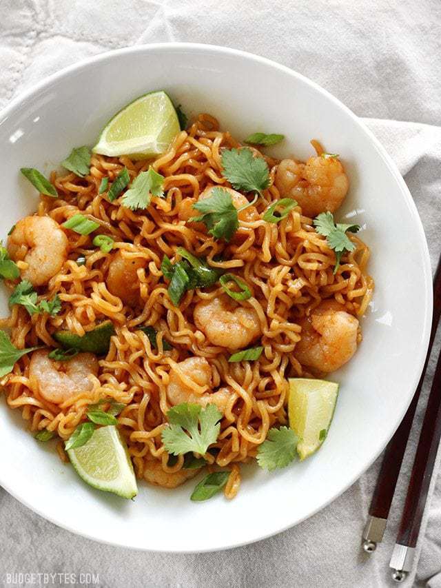 These spicy Lime Shrimp Dragon Noodles are a fast, easy, and inexpensive alternative to take out. This version features tender shrimp and fresh lime. BudgetBytes.com Overhead view of a bowl full of Lime Shrimp Dragon Noodles garnished with lime wedges and fresh cilantro. Chopsticks on the side.