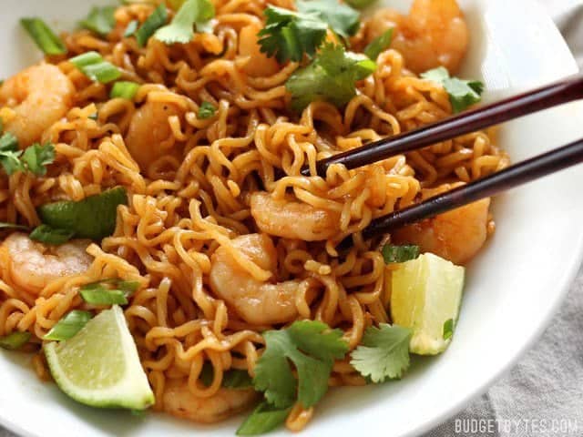 These spicy Lime Shrimp Dragon Noodles are a fast, easy, and inexpensive alternative to take out. This version features tender shrimp and fresh lime. BudgetBytes.com Close up of Lime Shrimp Dragon Noodles in the bowl with chopsticks picking up a piece of shrimp and some noodles