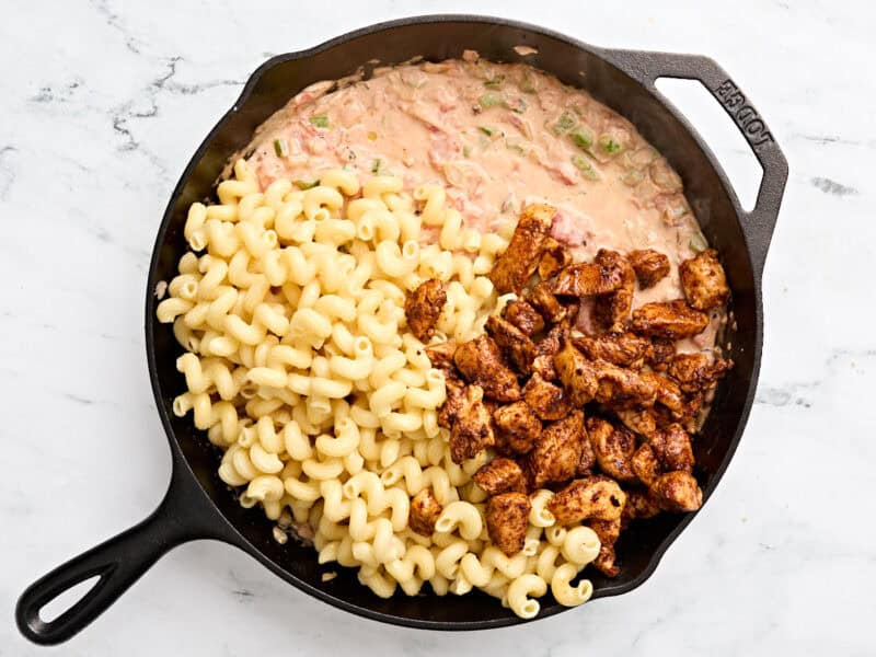 Fajita chicken and cooked pasta added to a creamy sauce in a skillet to make fajita pasta.