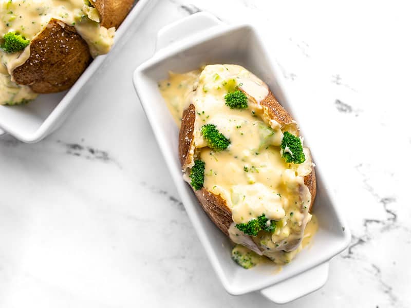 Broccoli Cheddar Stuffed Potatoes are a vegetarian comfort food classic. Perfectly baked russet potatoes with a rich and creamy broccoli cheese sauce! BudgetBytes.com Overhead view of a broccoli cheddar stuffed potato in an individual white ceramic casserole dish