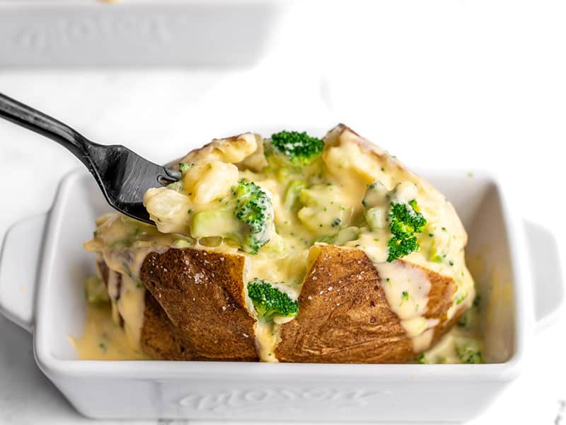 Broccoli Cheddar Stuffed Potatoes are a vegetarian comfort food classic. Perfectly baked russet potatoes with a rich and creamy broccoli cheese sauce! BudgetBytes.com A fork digging into a broccoli cheddar stuffed potato
